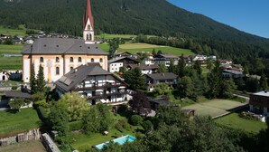 Eine Kirche mit einem hohen Turm, umgeben von Wohngebäuden und einer Bergkulisse.