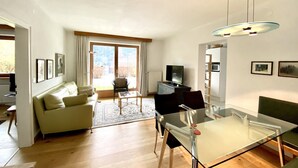 Ein modernes Wohnzimmer mit einem Glastisch, einer Couch, einem Fernseher und Blick durch große Schiebetüren.