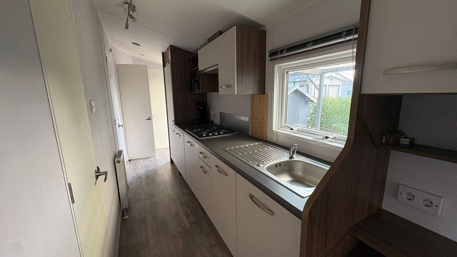 A compact kitchen with a built-in sink, a window above the sink, and a door leading to another room.