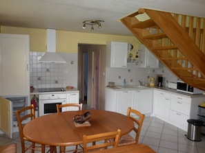 A kitchen with white cabinets, a wooden dining table, and a staircase.