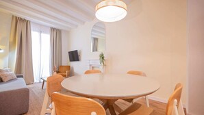 Una sala de estar moderna con una mesa de comedor redonda, sillas de madera, un sofá, un televisor de pantalla plana y un espejo grande.
