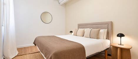 A bedroom with a bed, bedside tables, a mirror, and a rug.