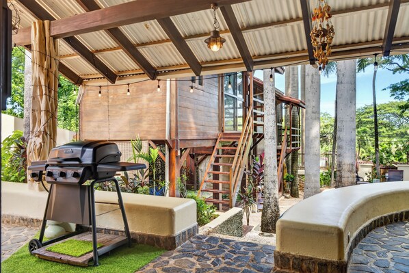 Un espacio al aire libre techado con una parrilla, una casita de juegos de madera y un suelo de baldosas de piedra.