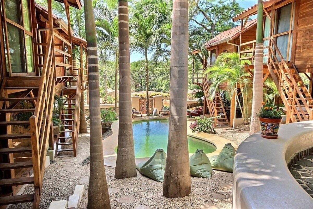 A wooden structure with a pool surrounded by palm trees and a garden.