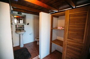 Un baño pequeño con lavamanos pedestal, inodoro y estantería de madera.