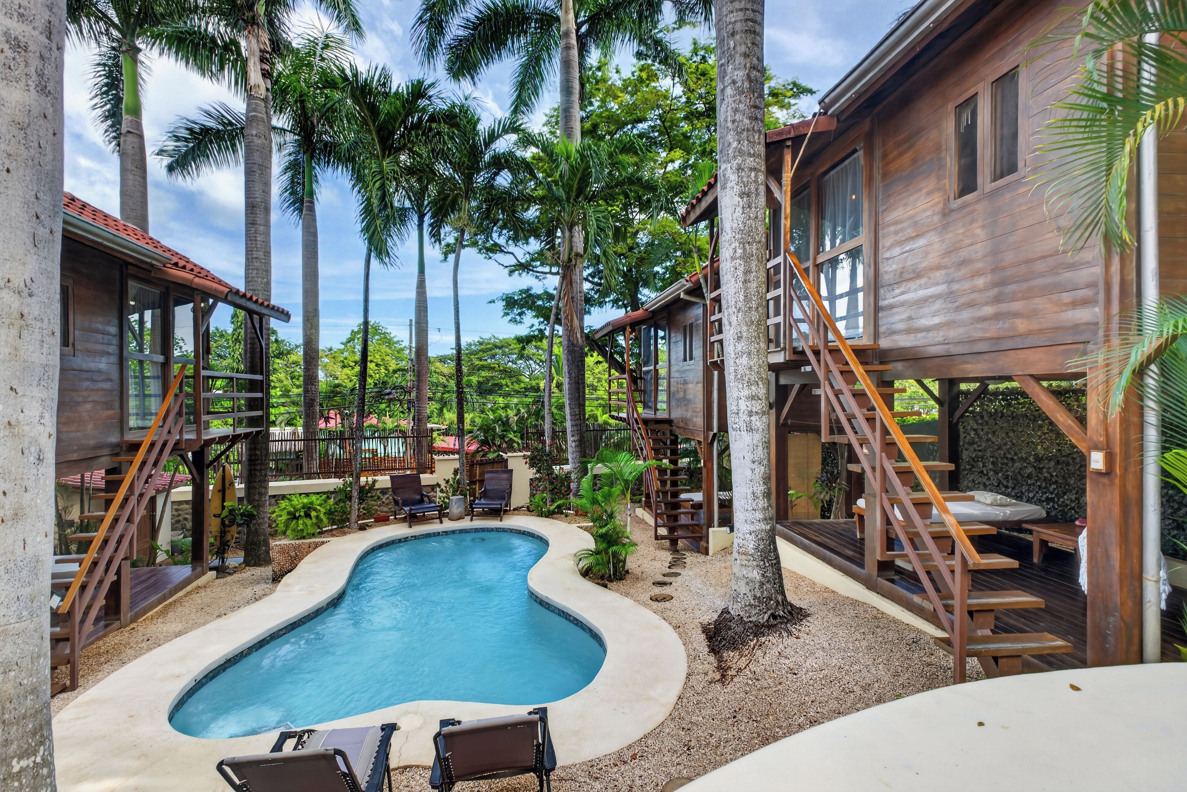 A pool area with wooden deck, lounge chairs, and a staircase leading to a wooden building.