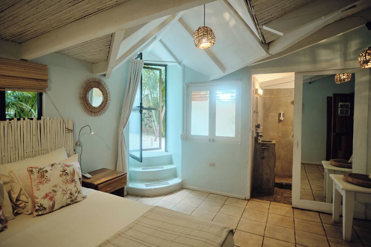 A bedroom with a bed, a nightstand, a mirror, and a window with curtains.