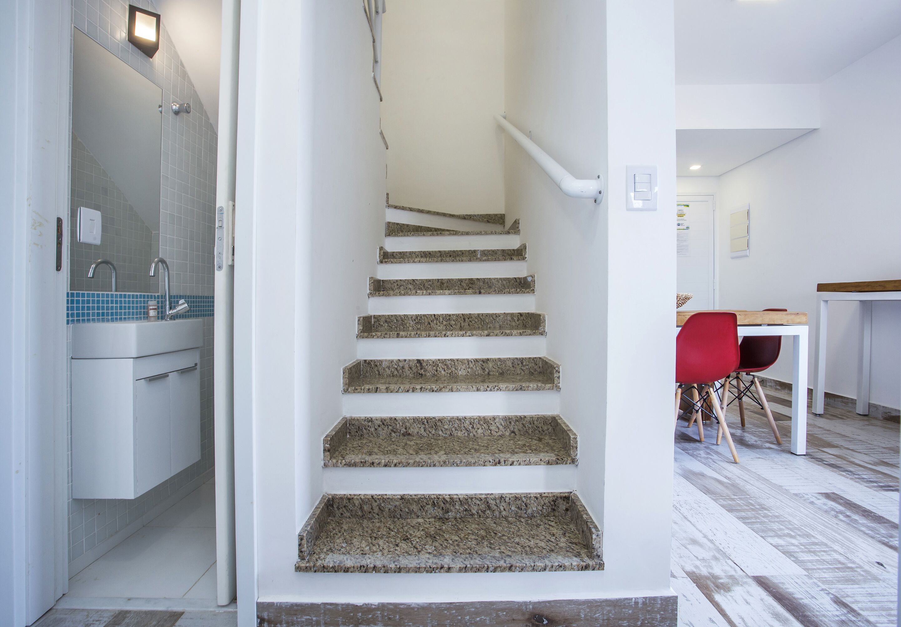 A staircase with a handrail, a bathroom with a sink and mirror, and a dining area with chairs and a table.