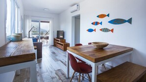 A modern dining area with a wooden table and red chairs, a TV, and a view through a glass door. - Ilhabela Beach Residences (Ilhabela)