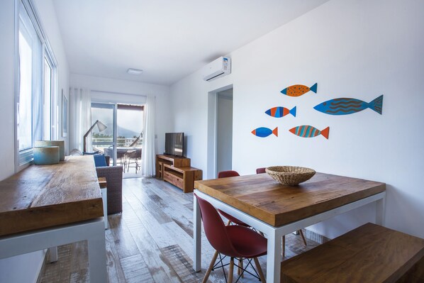 A modern dining area with a wooden table and red chairs, a TV, and a view through a glass door. - Ilhabela Beach Residences (Ilhabela)