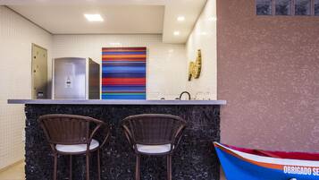 A modern kitchen with a black backsplash, stainless steel refrigerator, and two wicker bar stools.