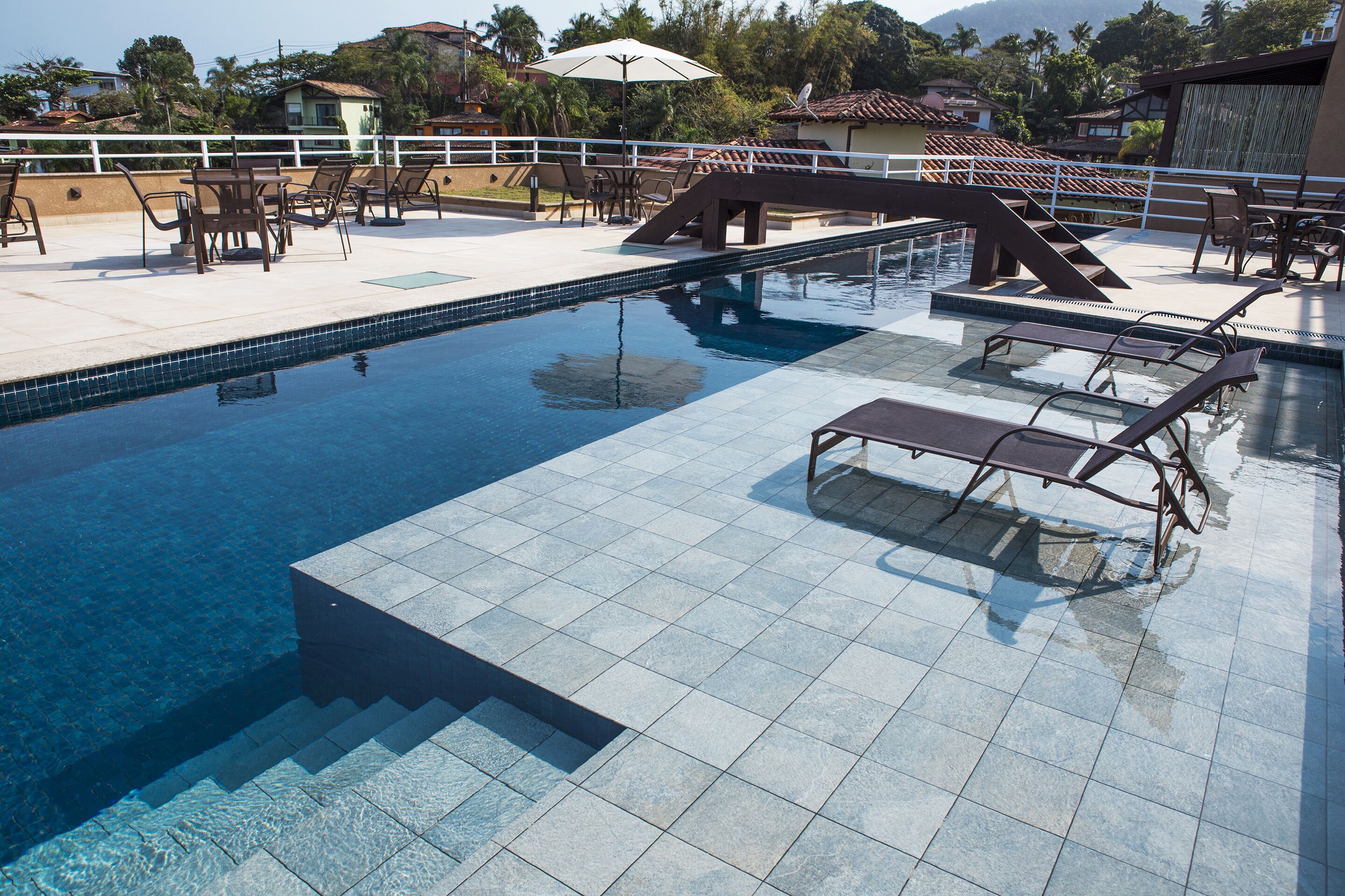 Una piscina con suelo de baldosas, tumbonas y un pequeño puente.