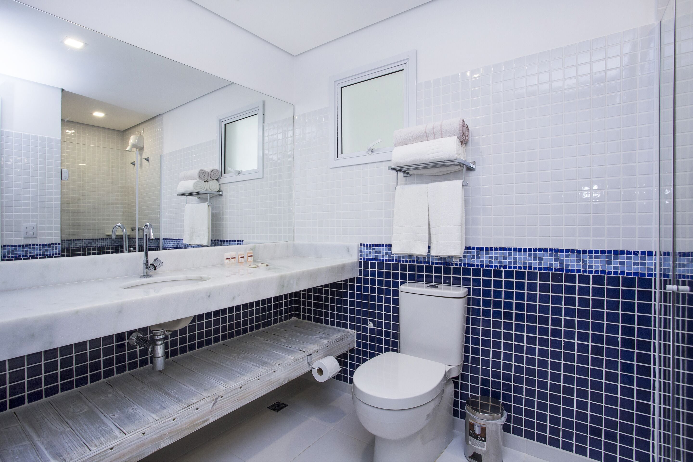 A bathroom with a white sink, a mirror, a toilet, and blue-tiled walls.