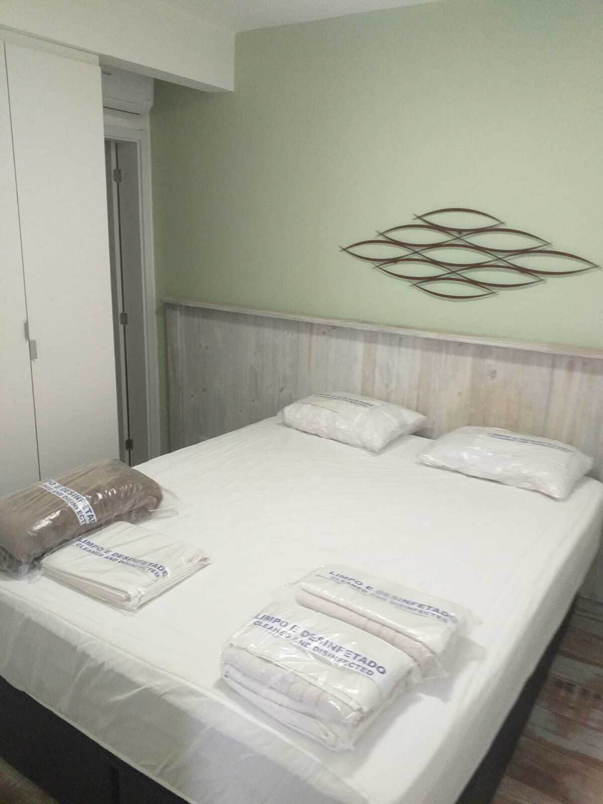 A neatly made bed with pillows and folded towels, a wooden headboard, and a decorative wall piece.