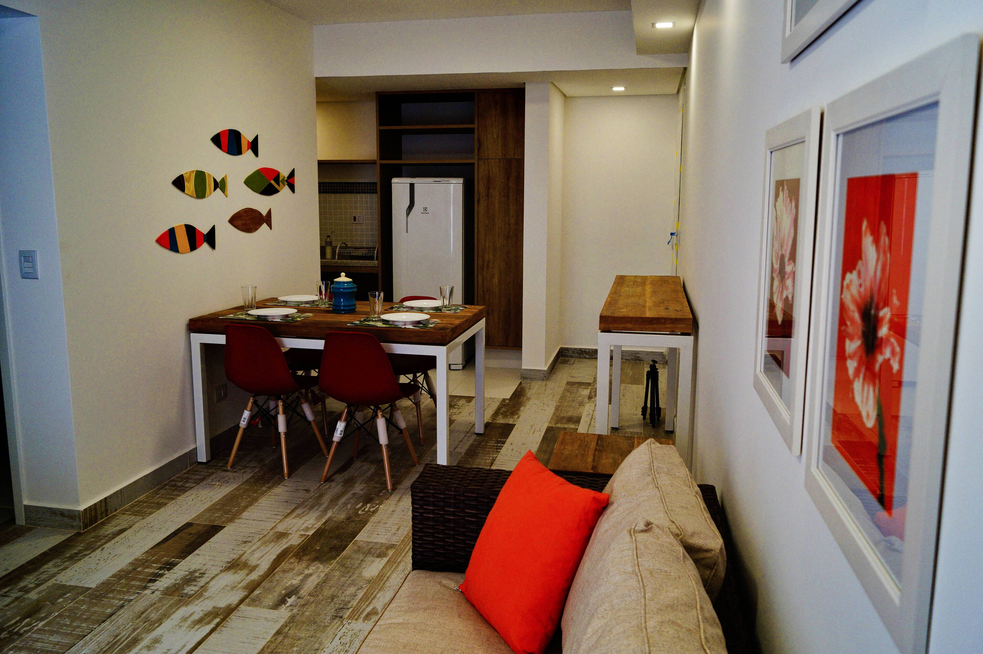 Un espace de vie compact comprenant un coin repas, une kitchenette et un canapé avec un coussin rouge.