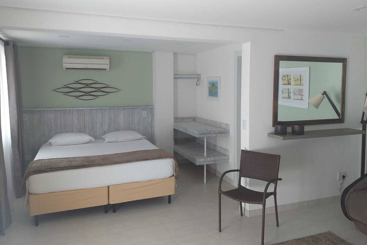 A bedroom with a bed, a chair, a desk, and a wall-mounted TV.
