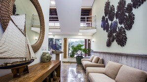 A lobby with a wooden bench, a sailboat model, a sofa, a large mirror, and a wall with leaf decorations. - Ilhabela Beach Residences (Ilhabela)