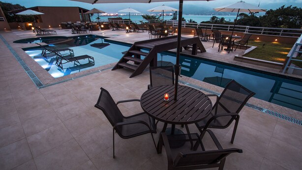 A poolside area with a table and chairs, a pool, and a view of the ocean. - Ilhabela Beach Residences (Ilhabela)