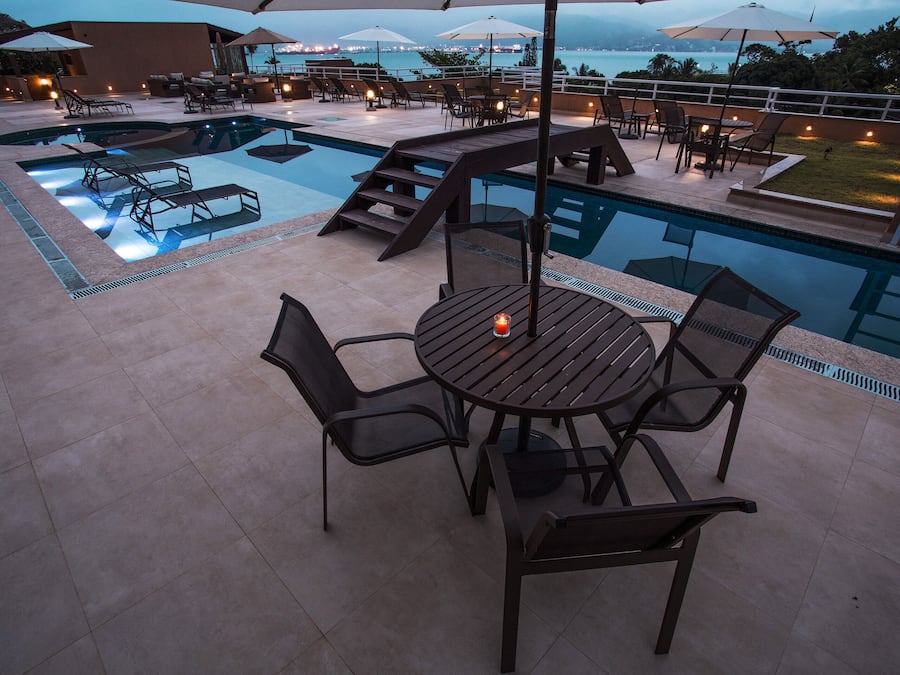 A poolside area with a table and chairs, a pool, and a view of the ocean.