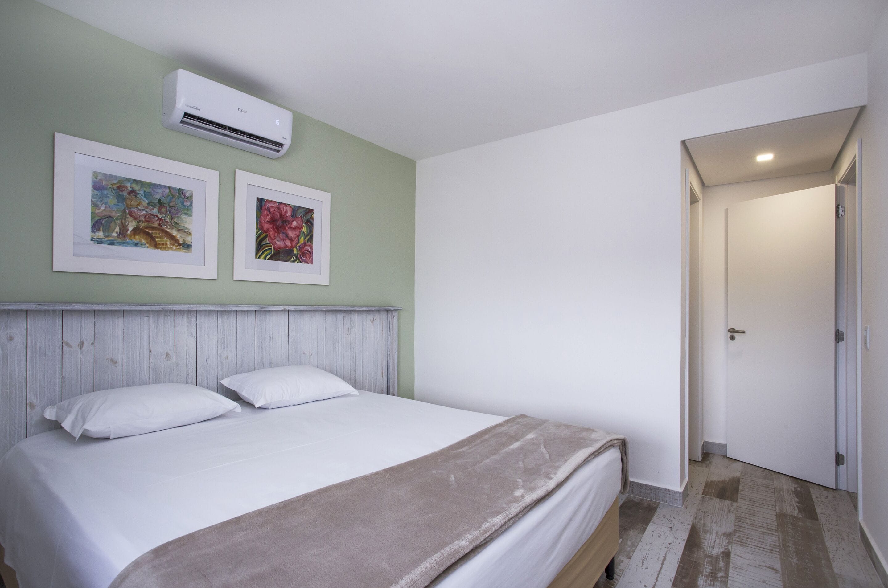 Un dormitorio con cama, cabecera, dos obras de arte enmarcadas y un equipo de aire acondicionado.