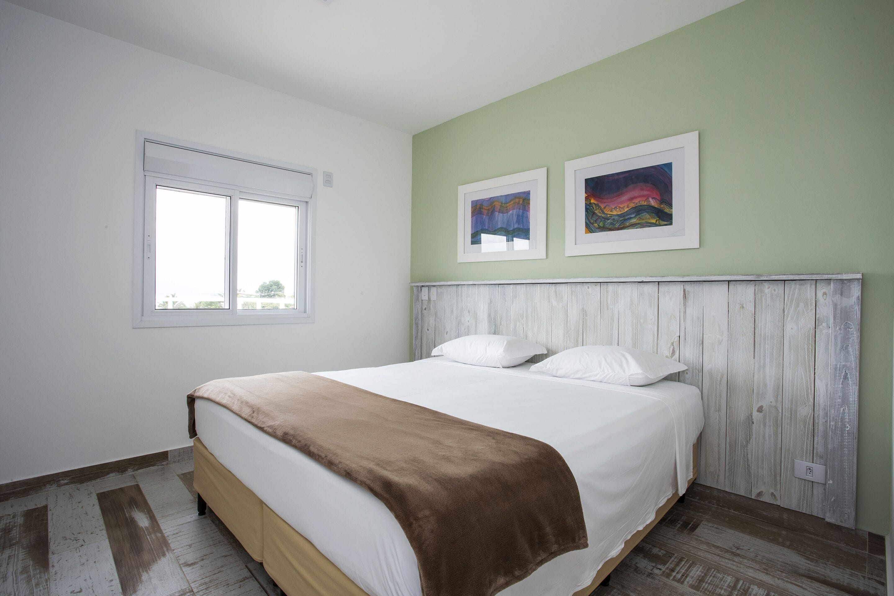 A bedroom with a bed, a window, and two framed pictures on the wall.