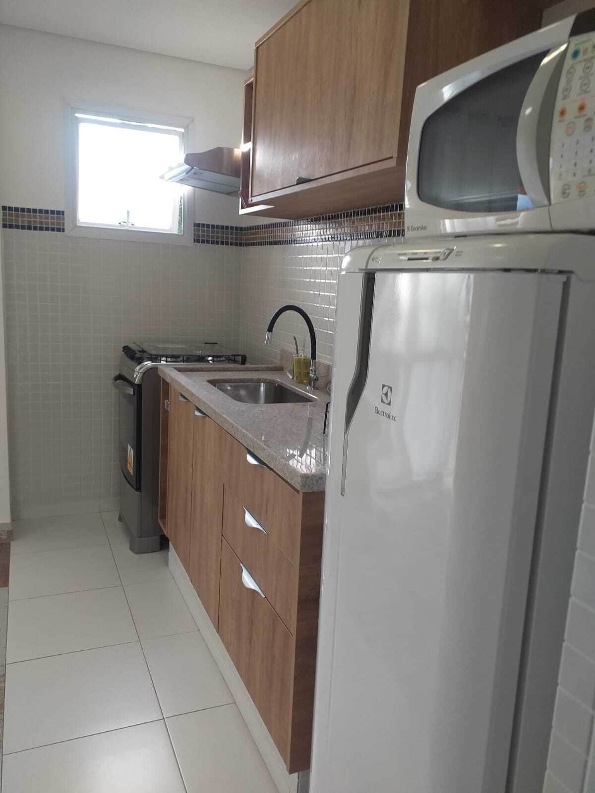 Una cocina con armarios de madera, un lavamanos de acero inoxidable, un microondas y un refrigerador.