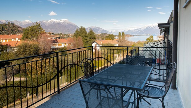 Ein Balkon mit Tisch und Stühlen mit Blick auf einen See und Berge.