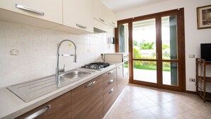 Eine moderne Küche mit Gaskochfeld, Spüle und Holzschränken. Ein großes Schiebeglastür führt auf eine Terrasse.
