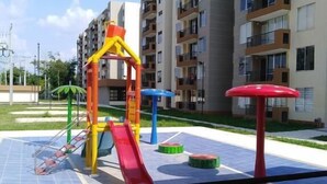 A playground with slides and climbing structures, surrounded by apartment buildings. - Lindo Apartamento (Ricaurte)