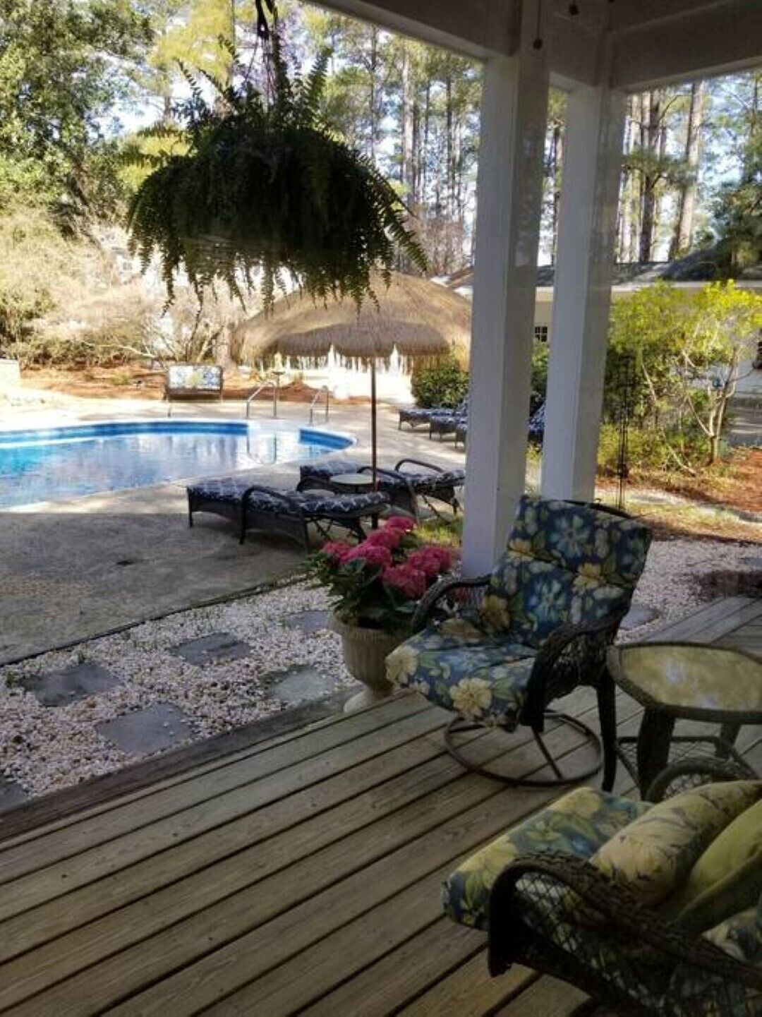 A covered outdoor area with a pool, lounge chairs, and a wooden deck.