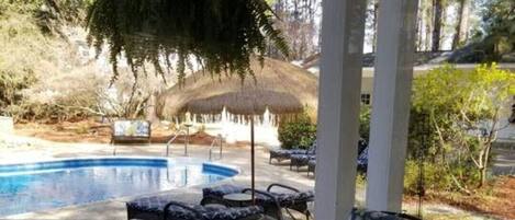 A covered outdoor area with a pool, lounge chairs, and a wooden deck.