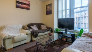 A living room with a sofa, a glass coffee table, a TV, and a window with a view of buildings. - Heart of Finnieston (Glasgow)