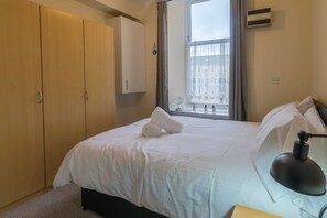 A hotel room with a bed, a desk with a lamp, a wardrobe, and a window with curtains. - Heart of Finnieston (Glasgow)