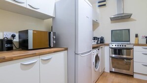 A compact kitchen with a white refrigerator, a toaster, a washing machine, and a stove. - Heart of Finnieston (Glasgow)