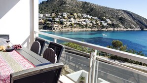 A balcony with a table set for two, overlooking a coastal town with buildings on a hillside and a boat on the water. - Spectacular Frontline Apt Sea Views 2mins Walk to Beach /5mins to Moraira (Moraira)
