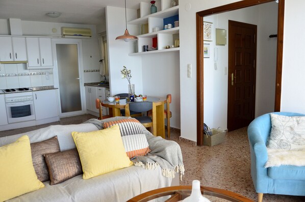 A living room with a sofa, a blue armchair, and a dining area with a table and chairs.