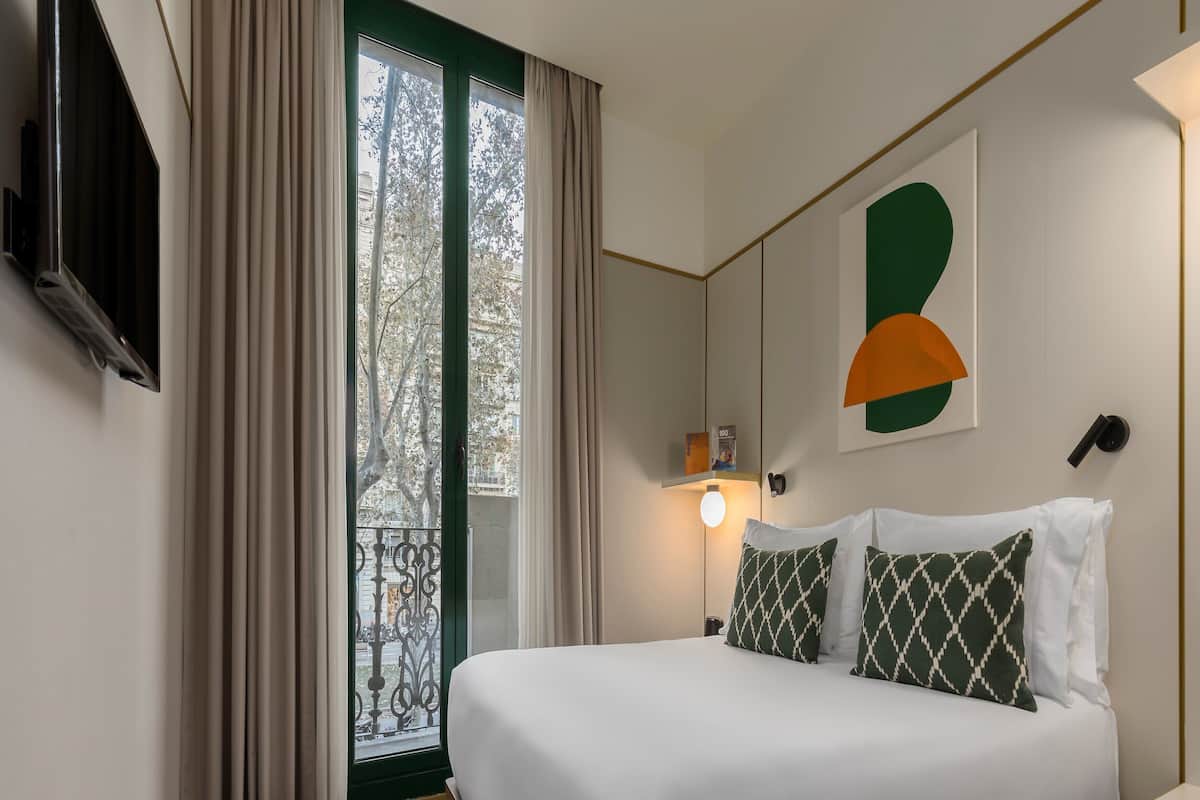 Ein modernes Hotelzimmer mit einem großen Bett, einem an der Wand befestigten Fernseher und einem Balkon mit Vorhängen.
