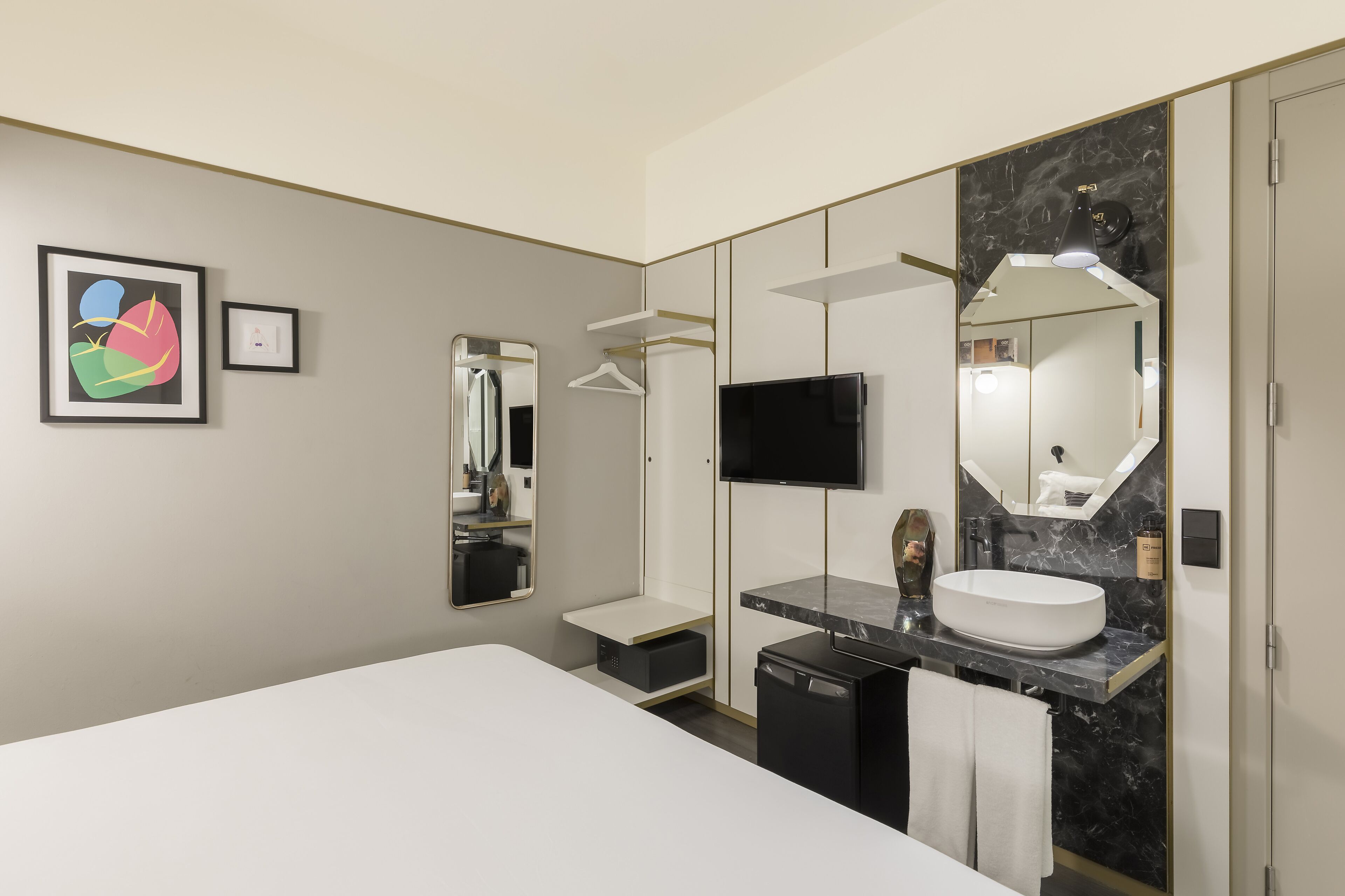 Moderni hotellihuone, jossa on suuri sänky, tyylikäs peilipöytä marmoritasolla, taulutelevisio ja suuri peili.