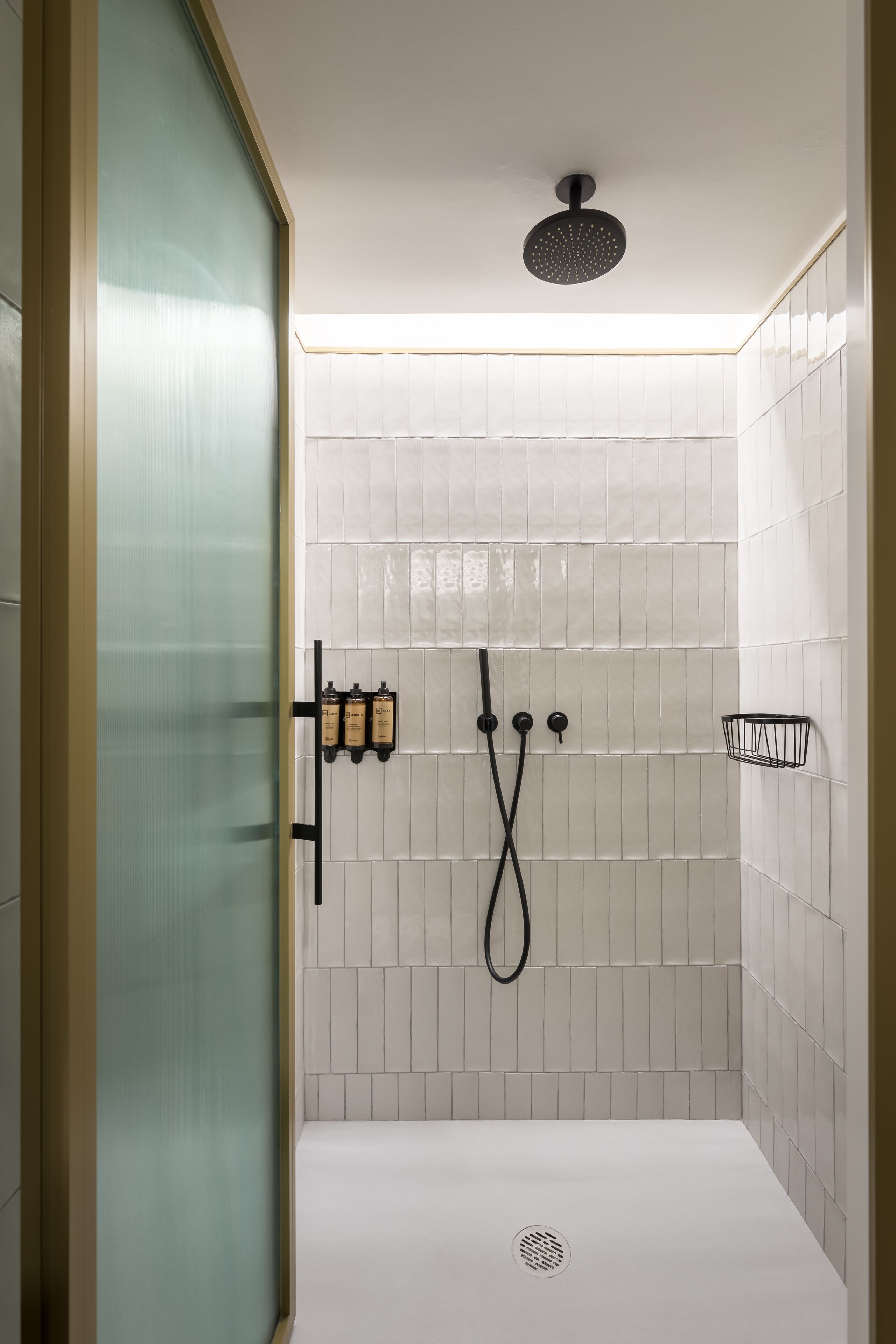 A modern shower with white tiles, a glass door, and a black showerhead.