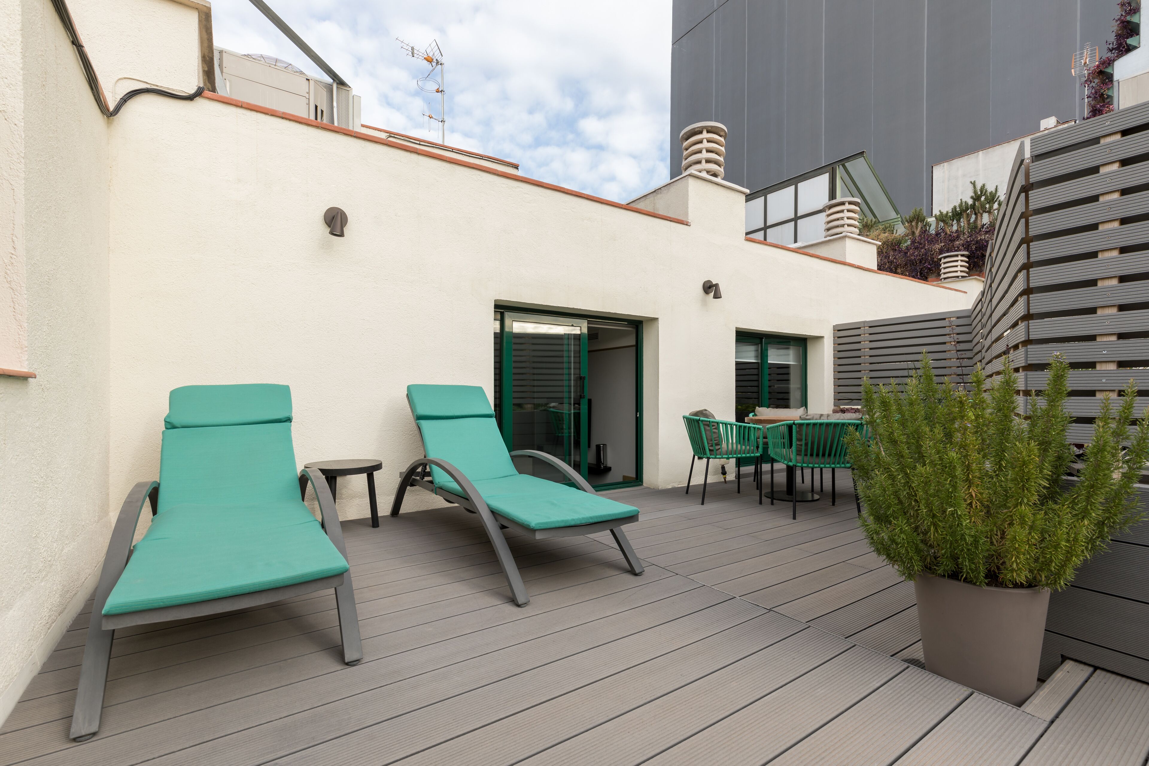 Una terraza en la azotea con dos sillones de descanso, una mesa y una planta en maceta.