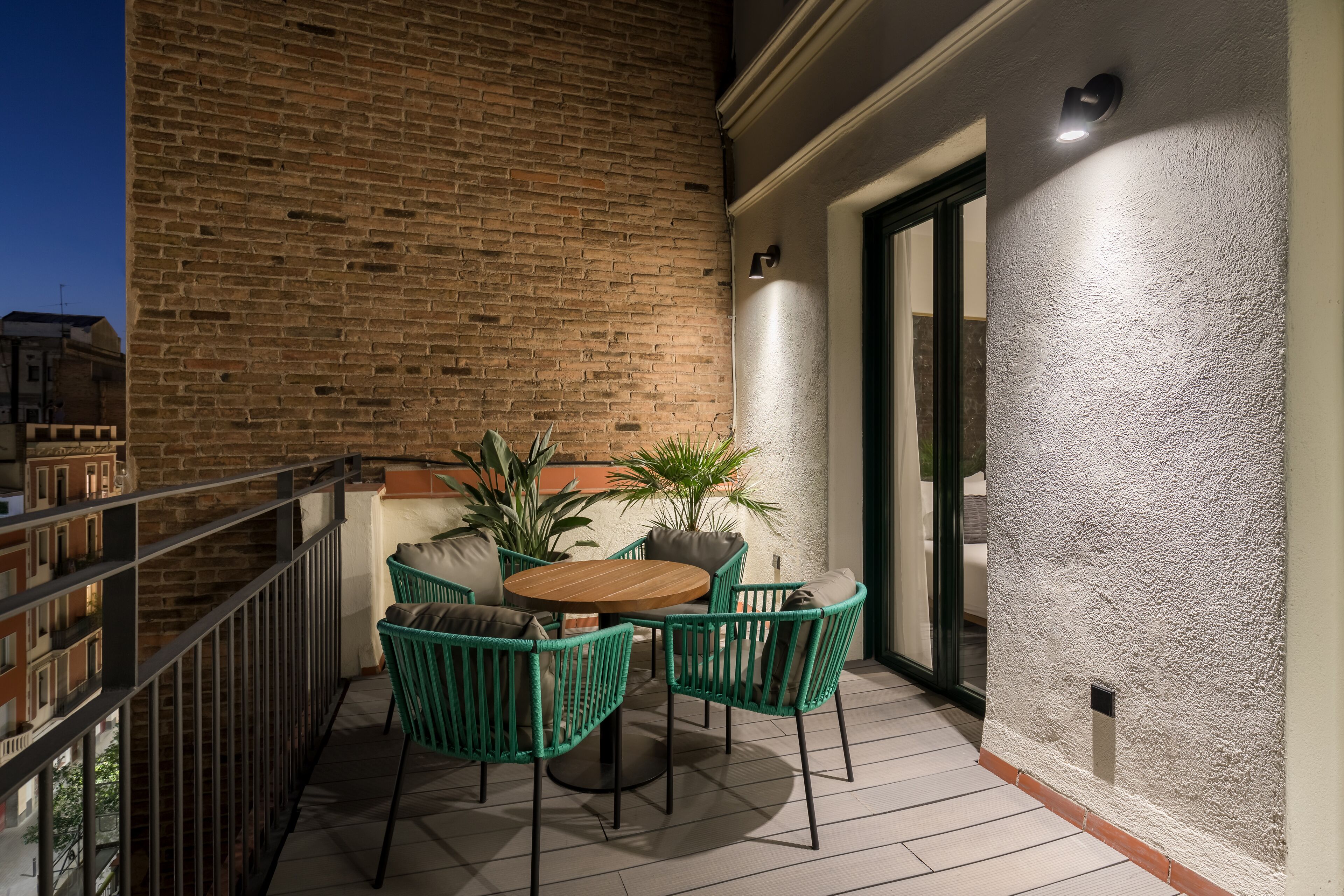 A balcony with a brick wall, a round wooden table, and green chairs.
