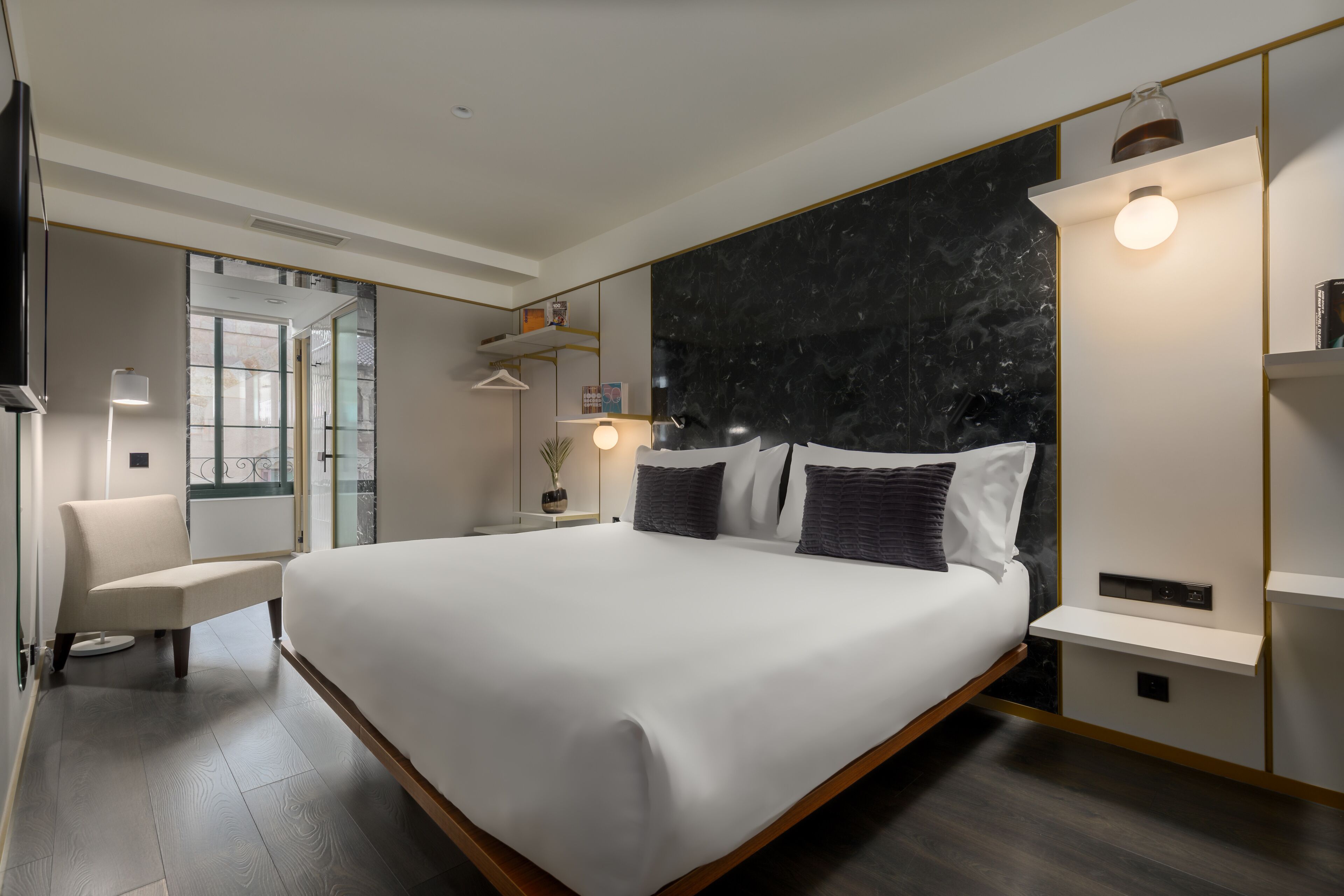 A modern hotel room with a large bed, a chair, a desk, and a marble accent wall.
