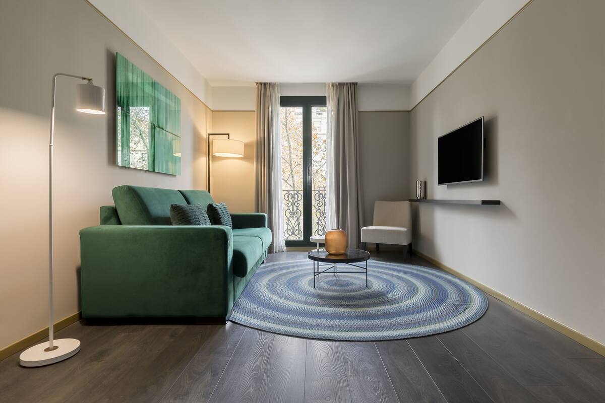 Ein modernes Wohnzimmer mit einem grünen Sofa, einem runden Couchtisch, einer Stehlampe und einem an der Wand montierten Fernseher.