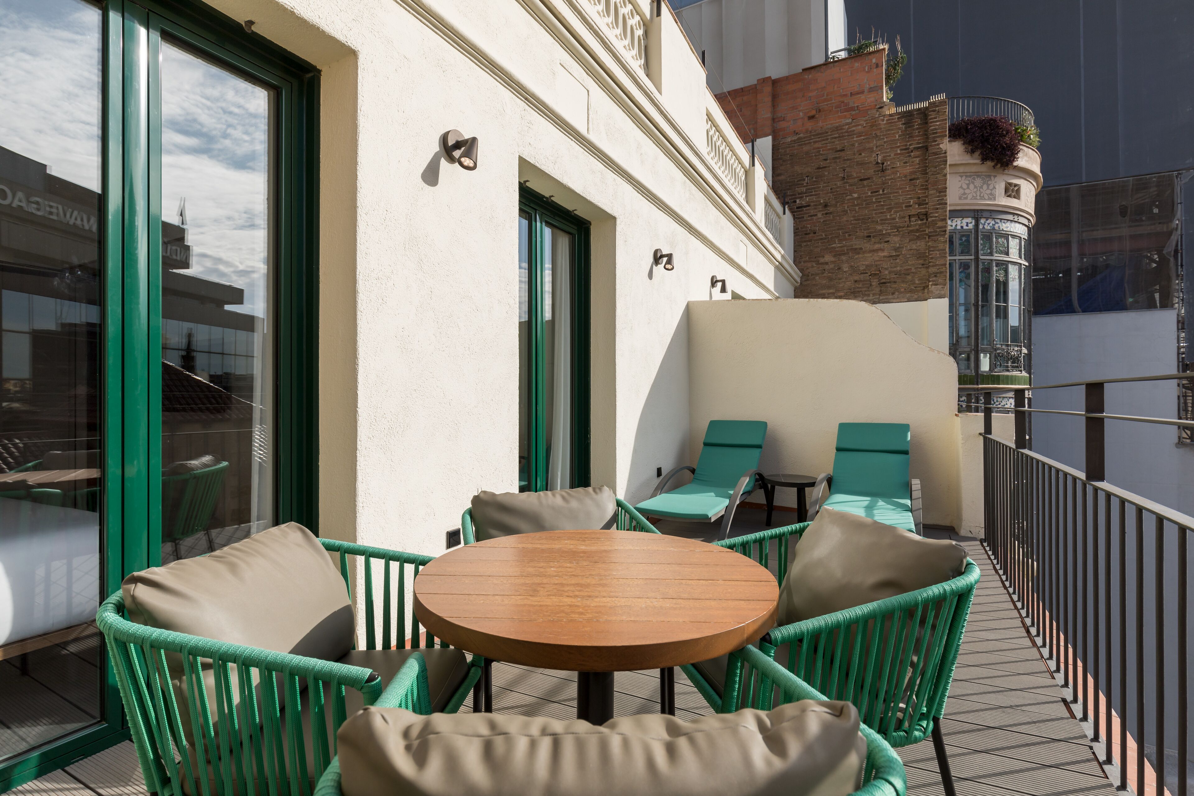 A balcony with wicker chairs and a round table, overlooking a cityscape.