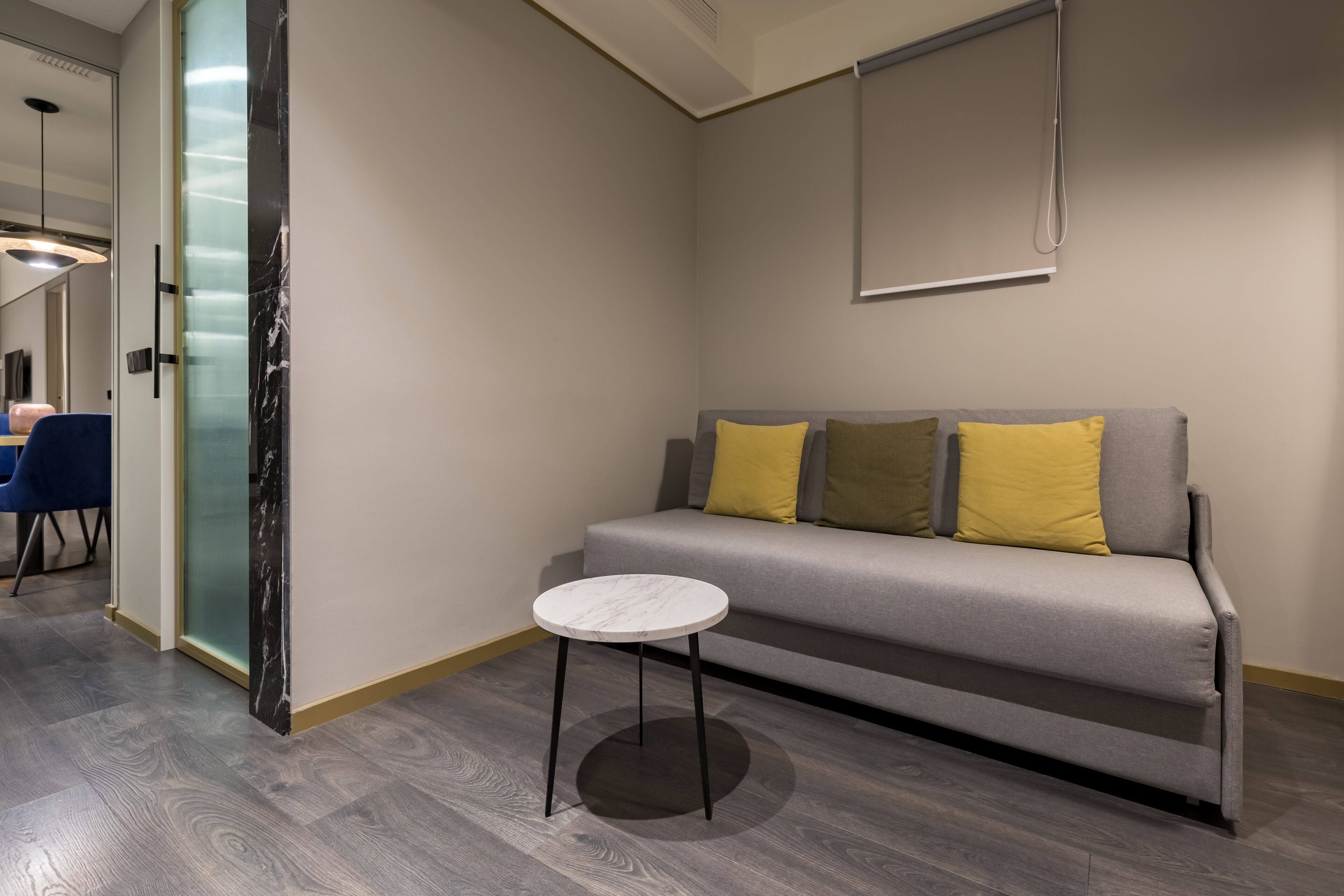 Un salón moderno con un sofá gris, una mesita redonda y un separador de vidrio.