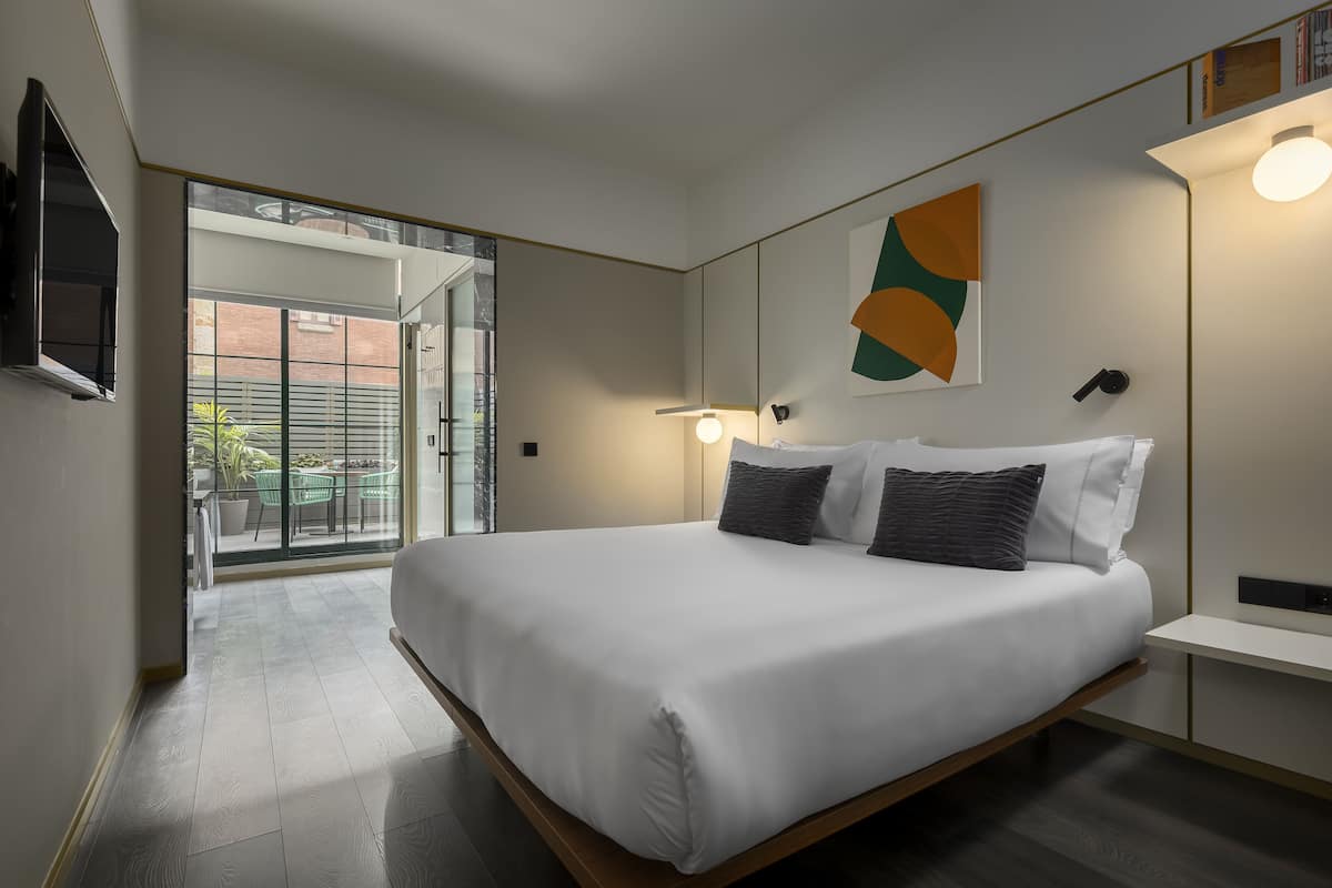 Ein modernes Schlafzimmer mit einem großen Bett, einem an der Wand montierten Fernseher und einer Glastür zum Außenbereich.