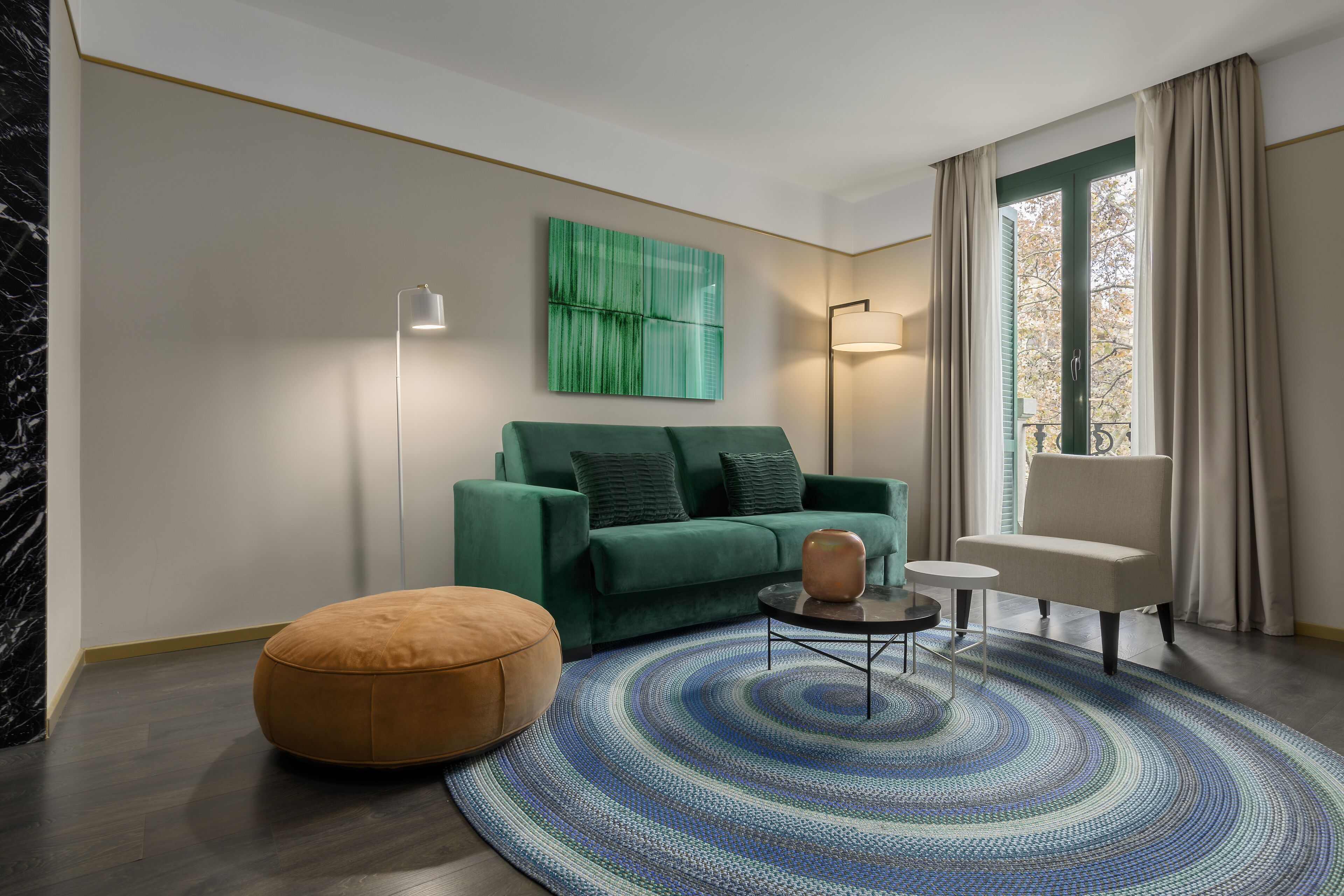 Un salon moderne avec un canapé vert, un pouf rond, une petite table et une lampe sur pied.