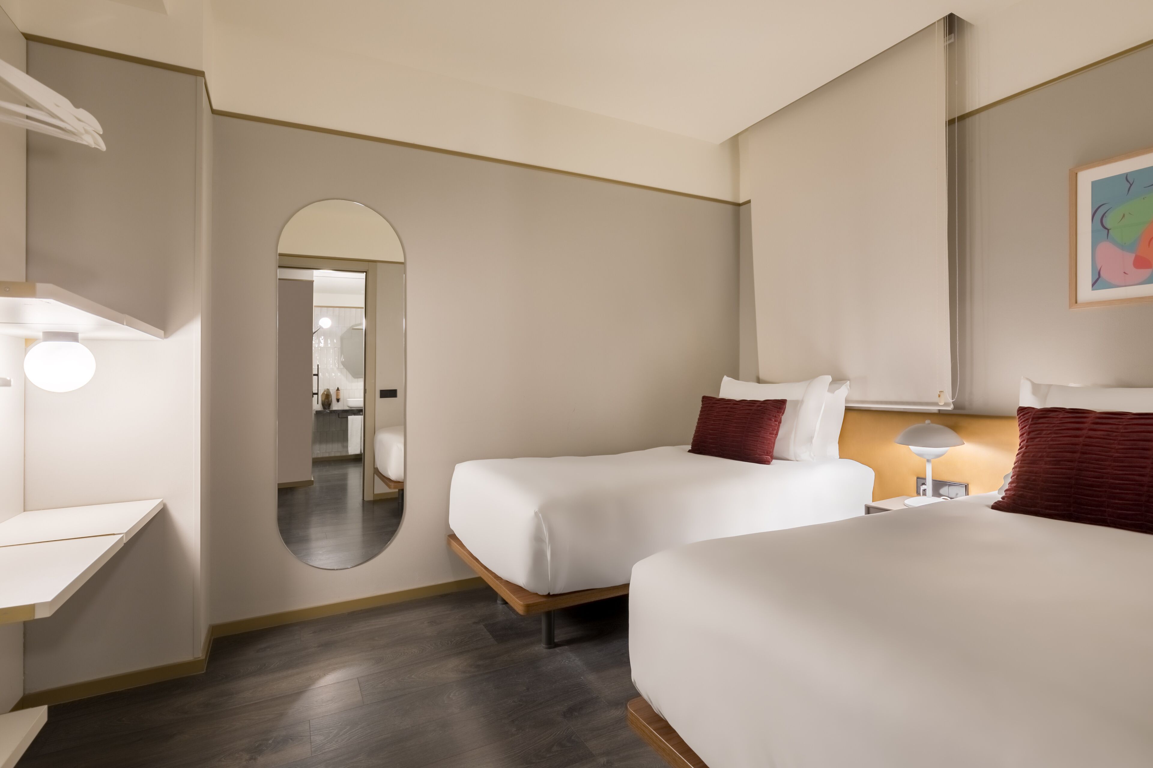Habitación de hotel con dos camas, un escritorio, un espejo y una lámpara.