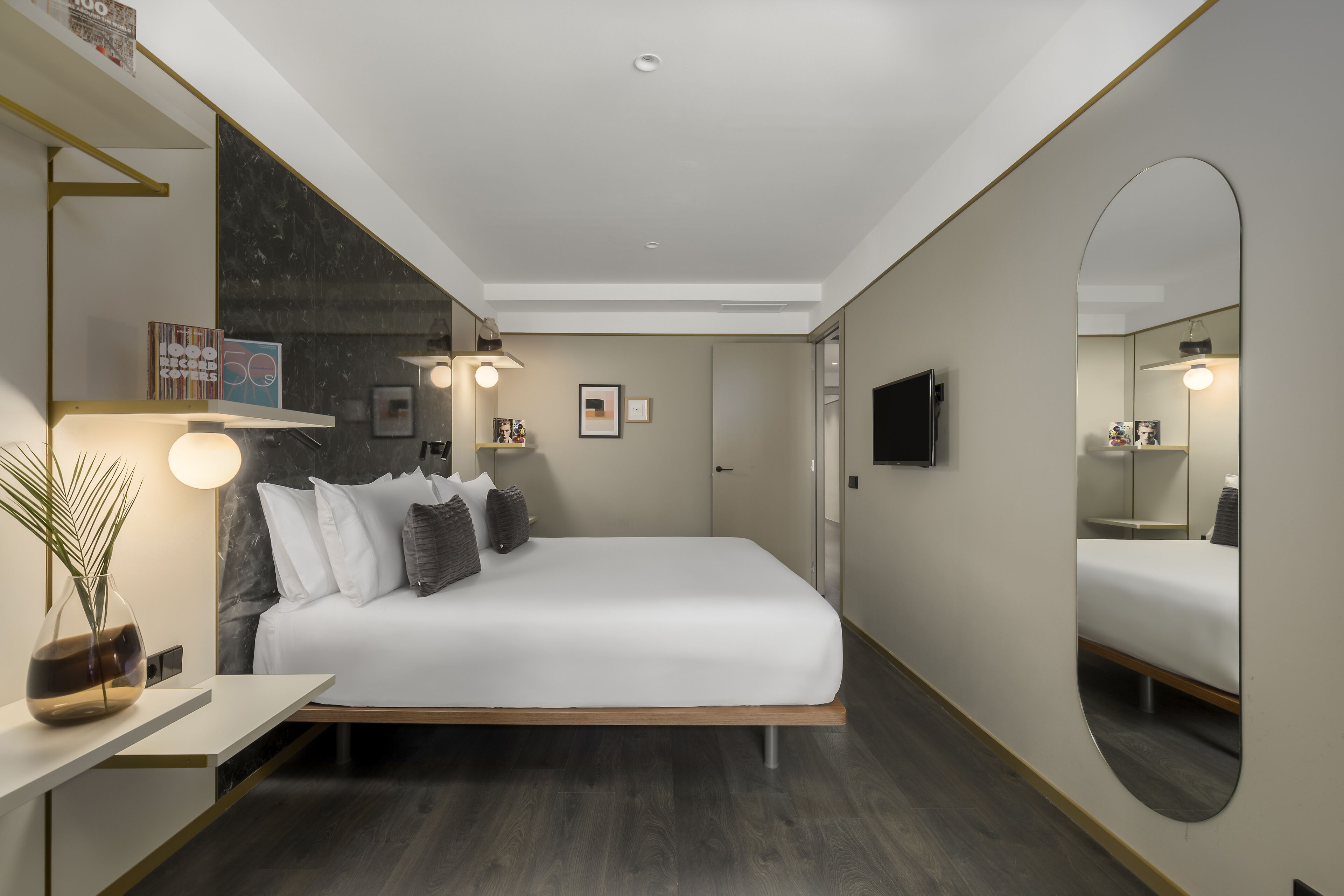 Ein modernes Hotelzimmer mit einem großen Bett, Nachttischen, einem Spiegel und einem Flachbildfernseher.