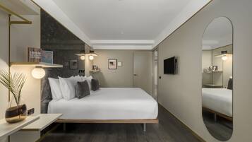 Una habitación de hotel moderna con una cama grande, mesitas de noche, un espejo y un televisor de pantalla plana.